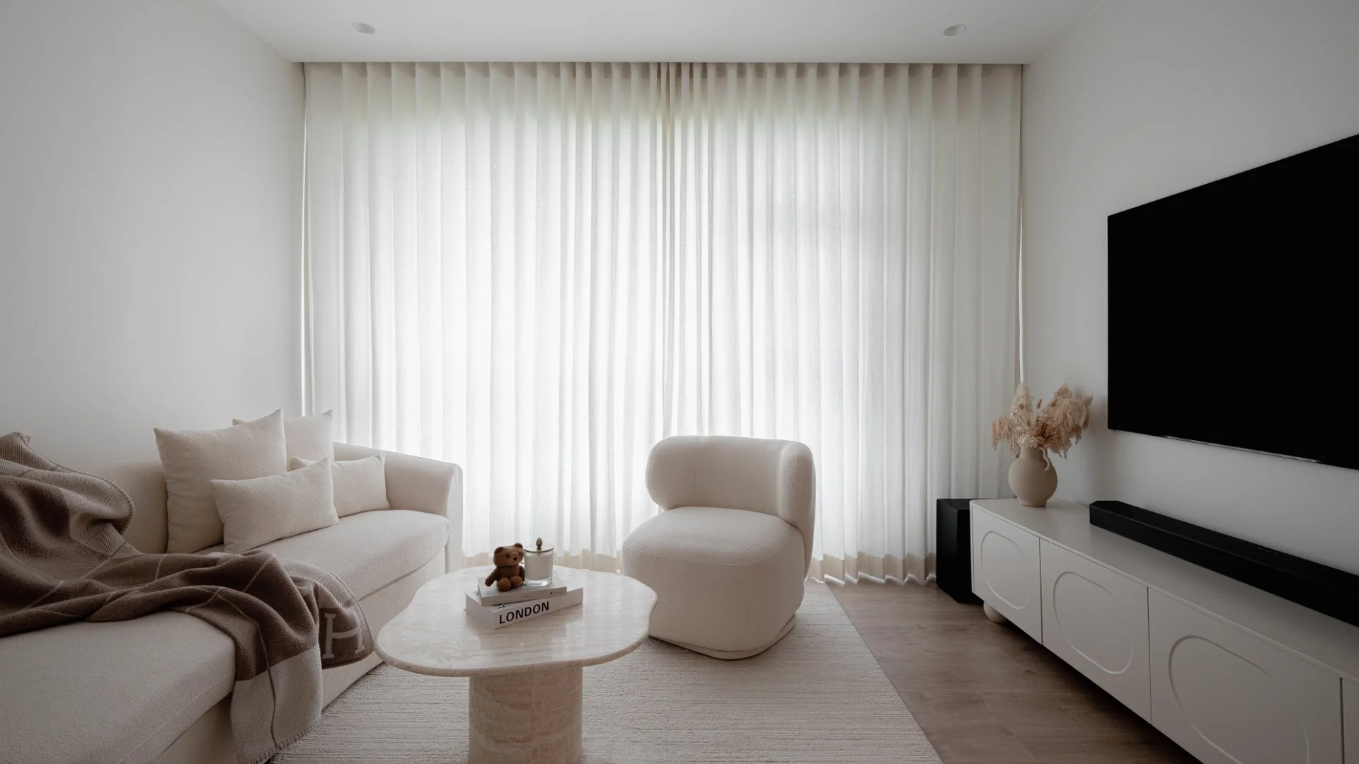 Serene minimalist living room with neutral tones, sheer curtains, and natural light by 6AM Spaces